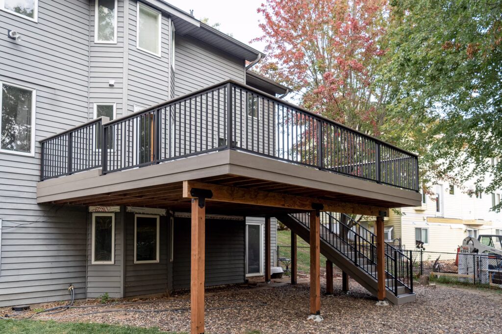 Ground level view of second-story gray Advanced PVC deck with stairs and wood frame. 