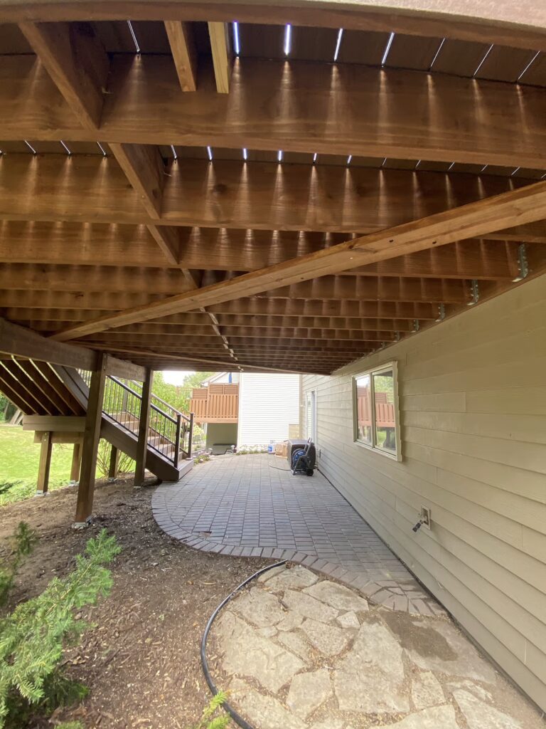 Underneath area of a deck with a paver patio and a staircase.