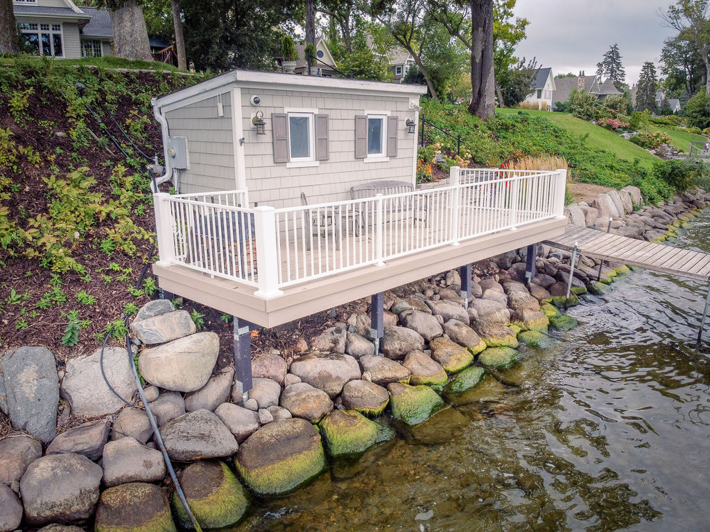 Angled view of lakeside boathouse with low-maintenance deck atop large stones. 