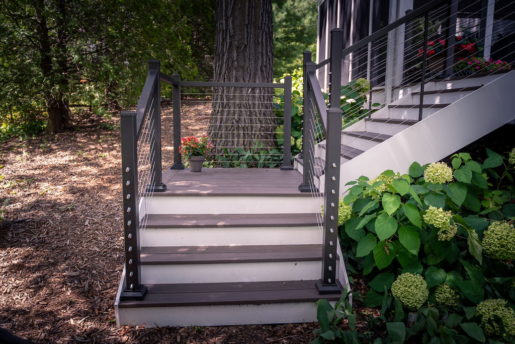 Lower portion of L-shaped deck staircase with PVC treads and platform, white PVC risers, and cable railing.