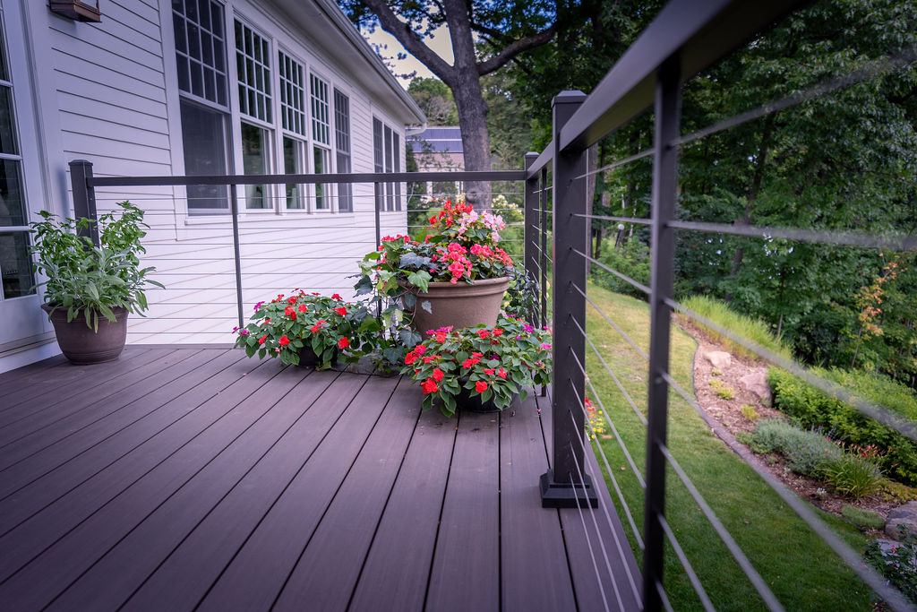Corner of low-maintenance deck with cable railing and red potted flowers.