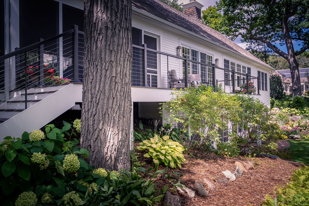 Composite deck with white trim and cable rail in a wooded backyard.