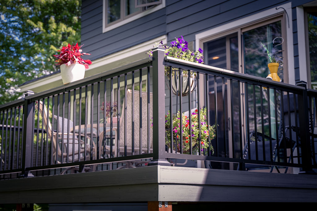 TimberTech Advanced PVC deck with aluminum railing with picket infill and integrated post cap lights, decorated with potted plants.