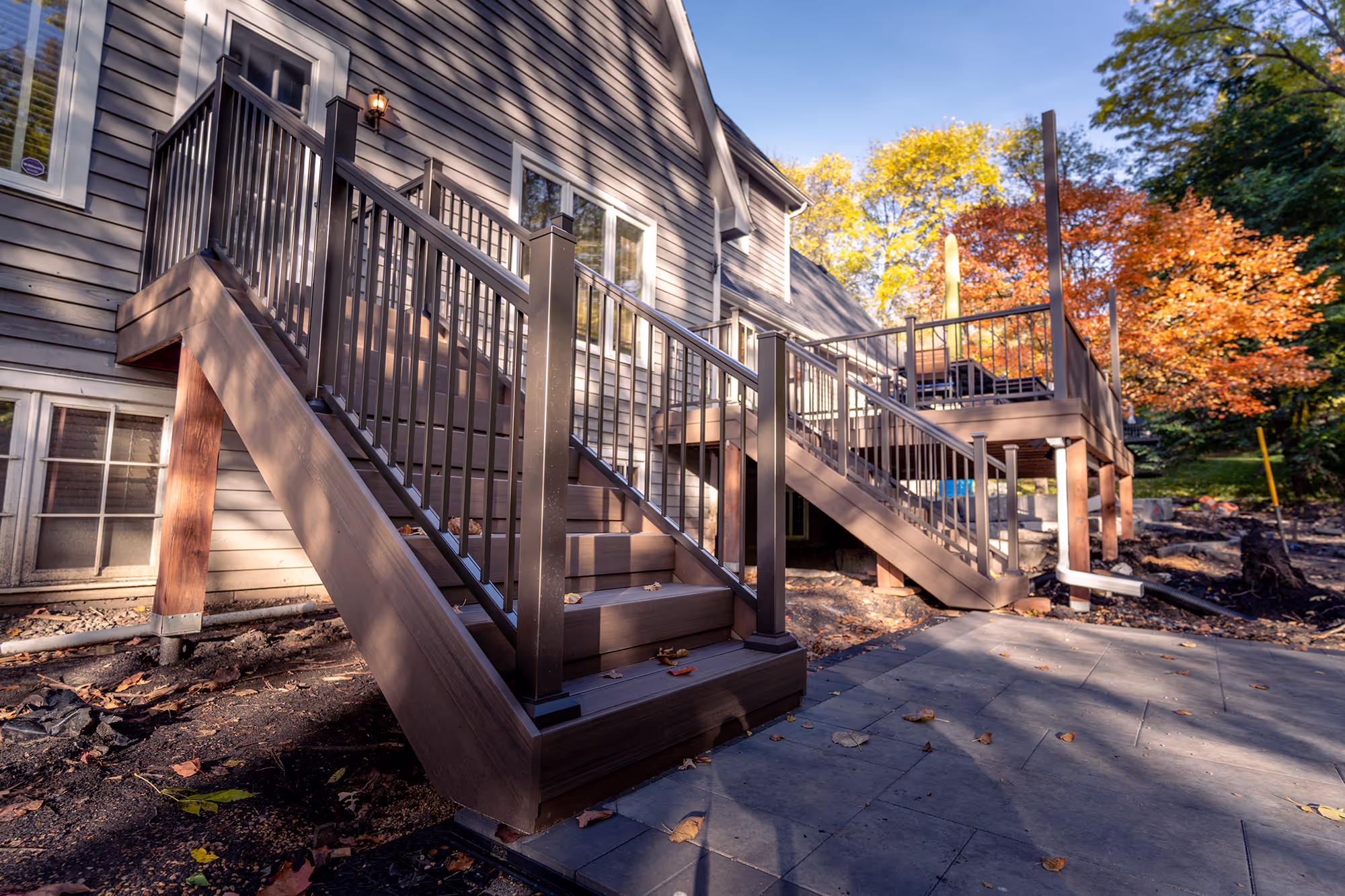 Two PVC staircases leading to a paver patio surrounded by fall foliage.