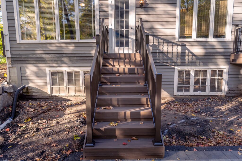 TimberTech Advanced PVC staircase with bronze aluminum railing leading from a house down to a square paver patio. 