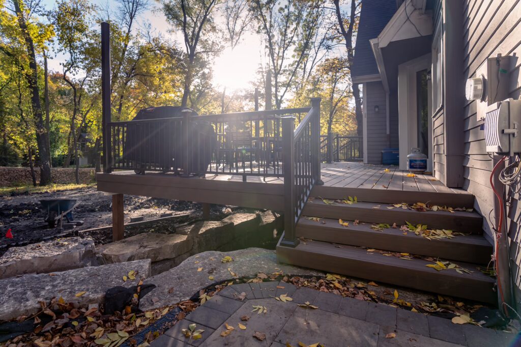 Additional short PVC deck staircase leading down to a brick paver patio on a sunny fall afternoon. 