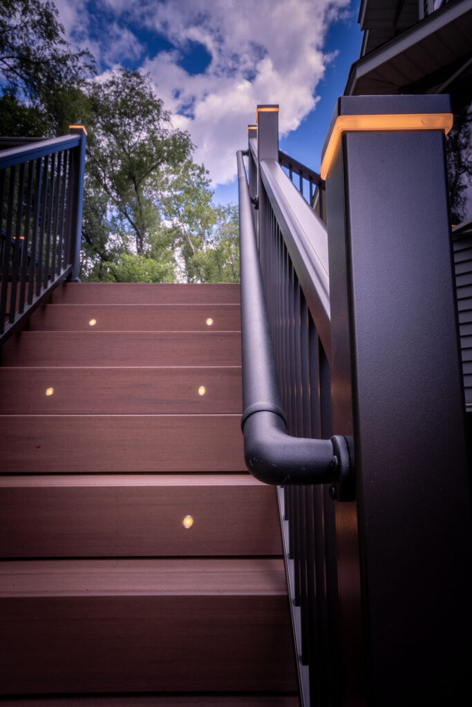 Detail view of low-maintenance deck staircase with aluminum rail with added ADA handrail, plus integrated stair riser lights and railing post cap lights. 