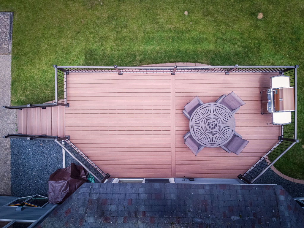Top aerial view of a low-maintenance deck with a staircase, a grill, and dining furniture. 