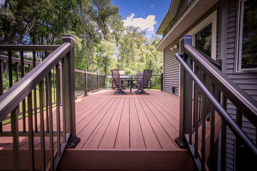 View from the top of composite deck staircase towards the open expanse of the deck with outdoor dining furniture. 