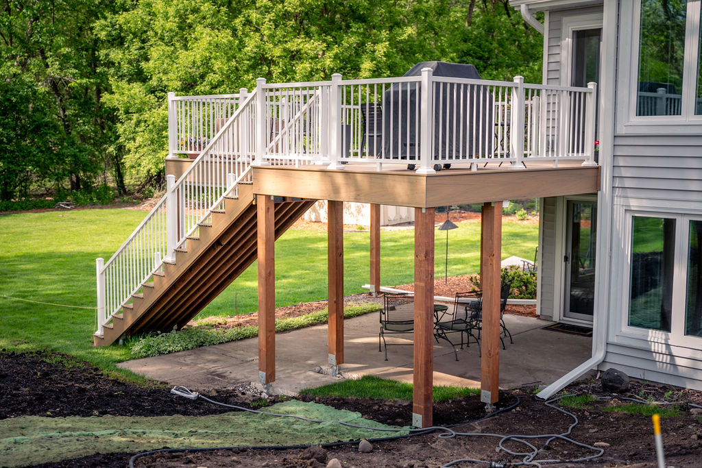 Rear view of low-maintenance TimberTech deck with white railing and wood frame over a cement slab patio. 