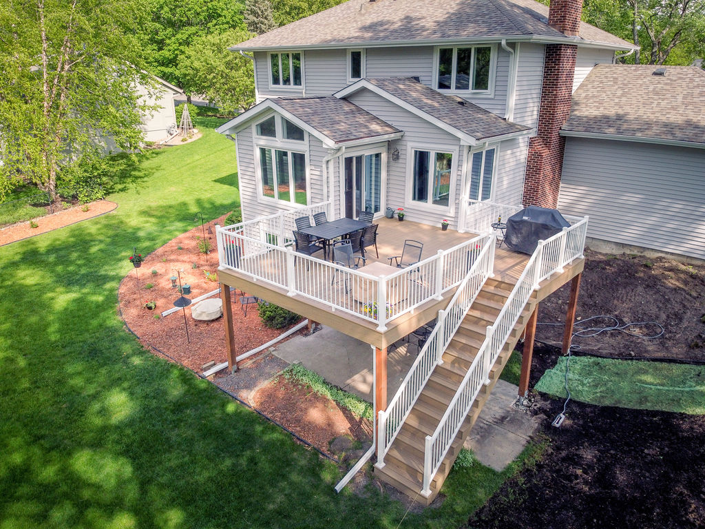 Aerial view of a composite deck with white railing and a staircase on the back side of a suburban house on a summer day.