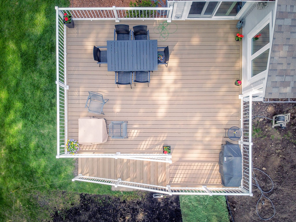 Top aerial view of a square composite deck with staircase and outdoor dining and seating furniture. 