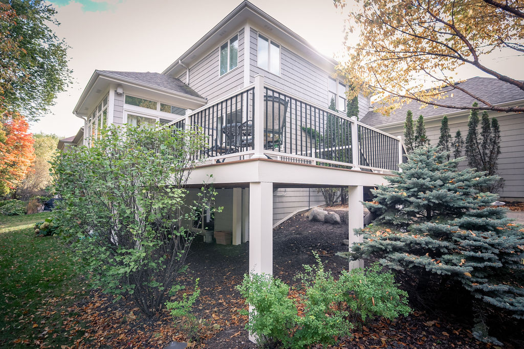 View of the back corner of a composite deck with white PVC fascia and post wraps, and black-and-white aluminum framing, surrounded by foliage.