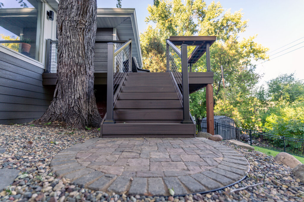 Low angle of composite deck stairs landing on a small round brick paver patio.