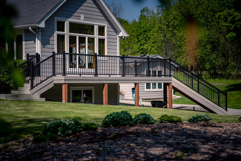 View of composite deck spanning the length of a house with staircases down both sides, viewed from a distance.
