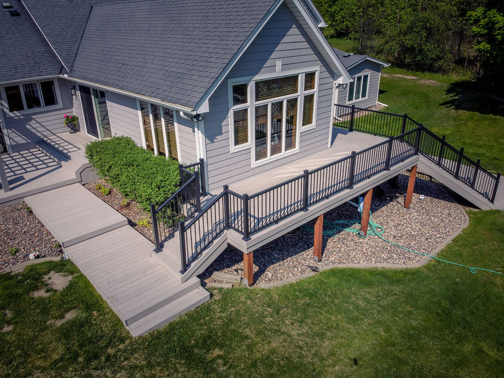 Aerial view of deck that wraps around a house, part of it is elevated and leads down to the main level on both sides.