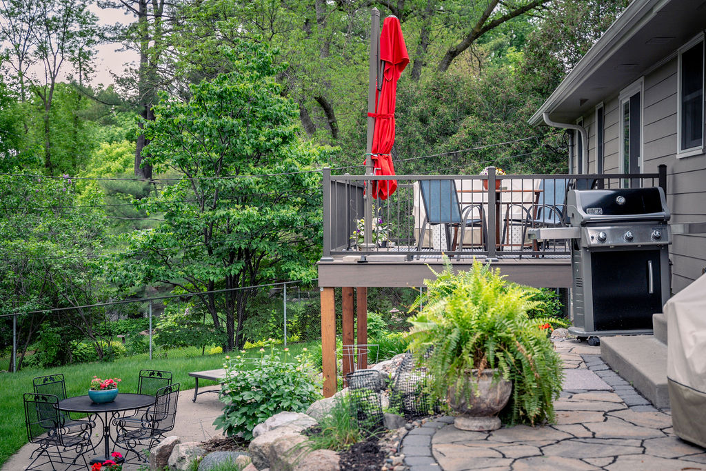 Opposite side view of a small furnished composite deck and surrounded by greenery.