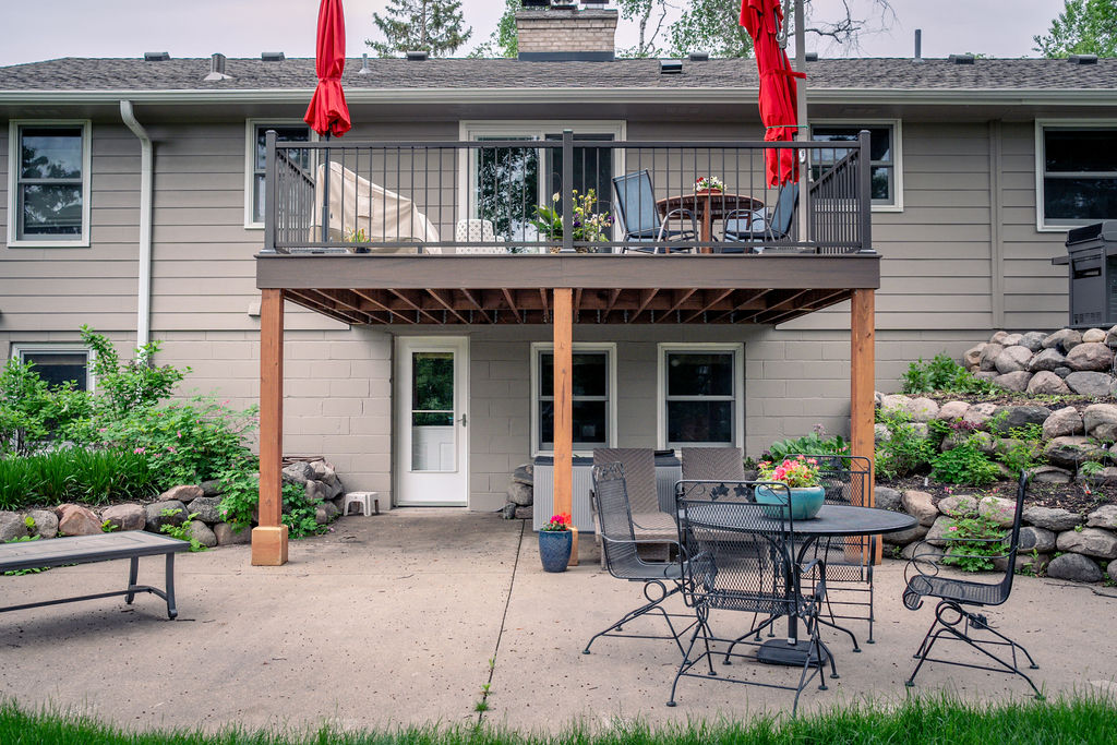 Front view of composite deck with no stairs and wood frame over a cement patio with furniture.