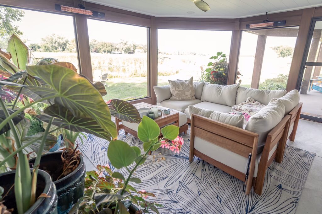 Inside of a low-maintenance screened-in porch with cozy furnishings and outdoor heaters near the ceiling.