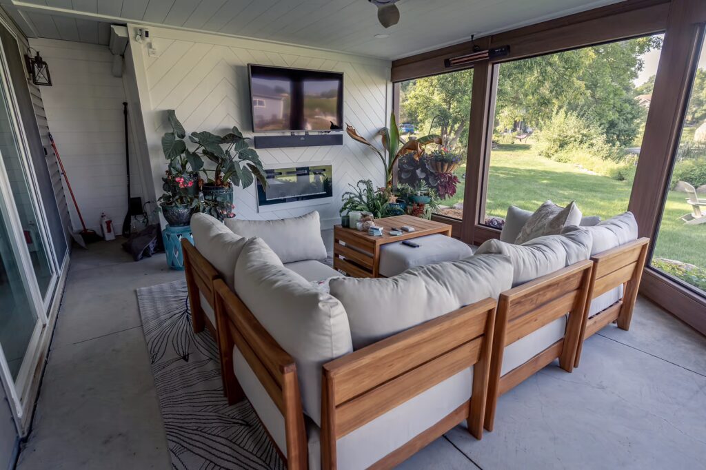 Screened-in porch with custom TV wall and cozy furnishings and plants. 