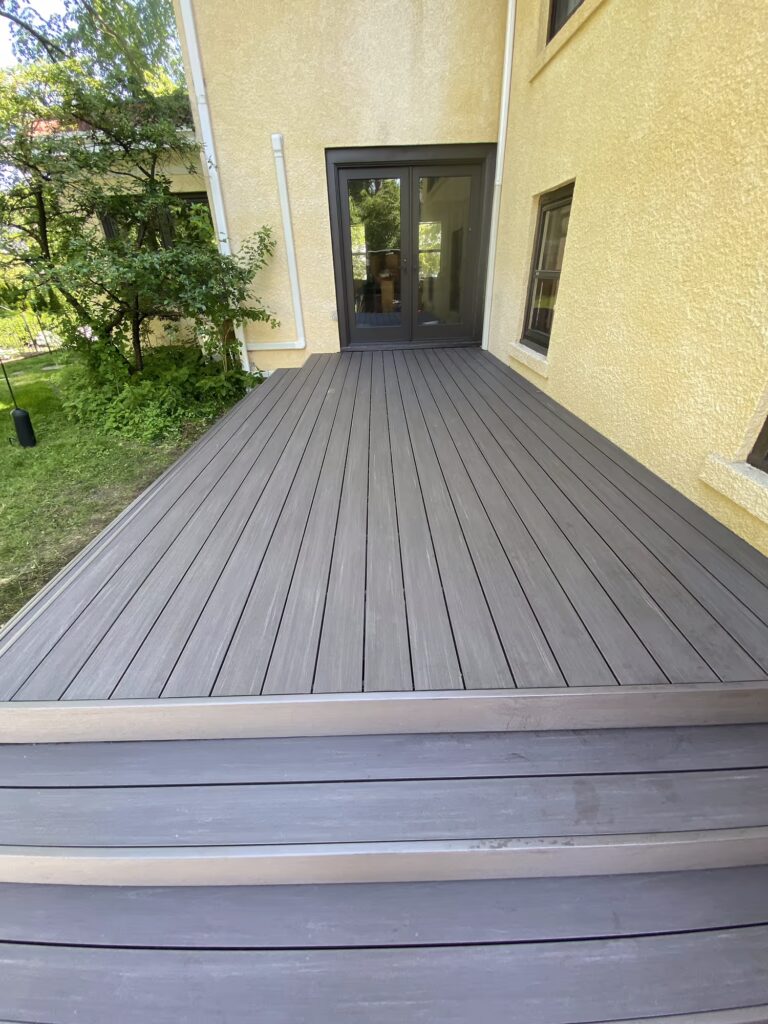 Low deck leading to a door on a yellow house.