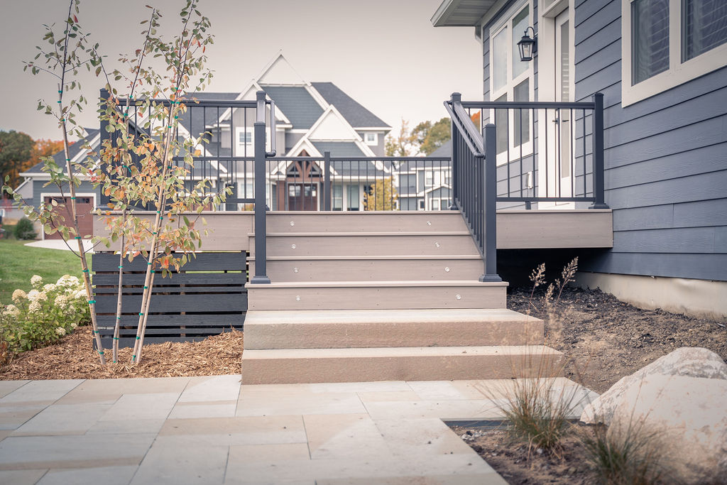 Low composite deck steps with integrated riser lights leading to two cement steps down to a paver patio. 