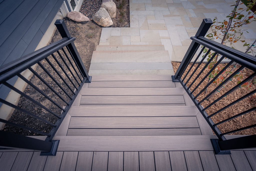 Top view of deck staircase on a low composite deck using TimberTech Composite decking and leading down to a paver patio. 