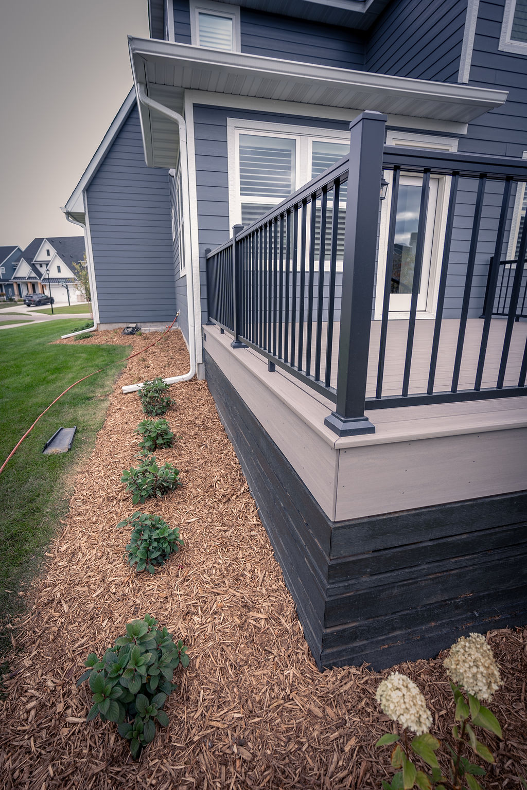 Side of a low TimberTech Composite deck with black aluminum railing and fresh landscaping with mulch. 