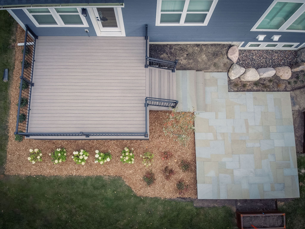 Top aerial view of a low composite deck leading down to a paver patio, all surrounded by mulch and freshly planted greenery.